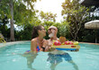 © romaset - A man and woman with tray of a fresh fruits in a swimming pool