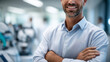 © Kateryna - Confident male doctor standing in exam room arms relaxed crop below eyes equipment softly defocused physician portrait faceless background defocused clean clinic