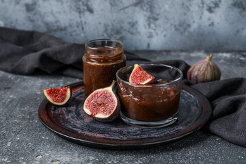 Wall Mural - Plate with glass and jar of sweet fig jam on grey grunge background