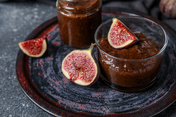 Wall Mural - Plate with glass and jar of sweet fig jam on grey grunge background