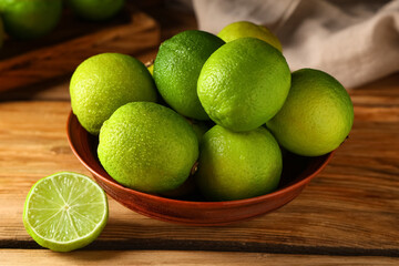 Wall Mural - Bowl with fresh ripe limes on wooden background, closeup