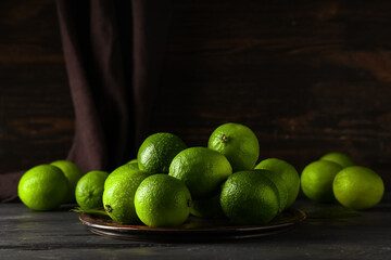 Wall Mural - Plate with fresh ripe limes on black wooden table