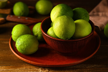 Wall Mural - Bowl and plate with fresh ripe limes on wooden background