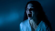 © Natali IQstock - Frightening spectral woman emerging from shadows, pale skin and black hair dripping with water, open mouth scream in eerie blue light. SEO: ghostly figure, horror movie concept, ha
