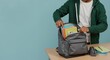 © Vyatcheslav - A young student packing his backpack with notebooks and school supplies on a desk. Preparing for college or a new semester. Back to school and education concept with copy space