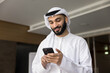 © fizkes - Smiling young middle eastern businessman hold smartphone read message text