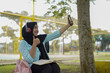 © Fajar - Young woman in hijab and headphones using a smartphone to record a video outdoors with a notebook and pen nearby, capturing a moment of content creation and learning in a casual setting