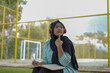 © Fajar - Serene young woman in a hijab and red headphones, deeply engrossed in reading a book while studying outdoors on a tranquil park bench, fostering knowledge and personal growth