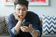 © chinnarach - close up young asian man with stress emotion on face with during hold smartphone to reading about bad comment on social media application or read news and rumor in home for people lifestyle concept