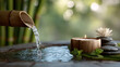 © visoot - Serene spa setting with bamboo water spout, flowing water, candle, stacked stones, green leaves, and white lotus flower