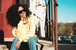 © halayalex - Beautiful woman with afro curls hairstyle.Smiling hipster model in yellow hoodie. Sexy carefree female posing on the street background in sunglasses. Cheerful and happy