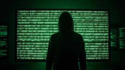 Mysterious hooded man stands in front of matrix style binary code wall. Hacker concept with digital data and network technology footage.