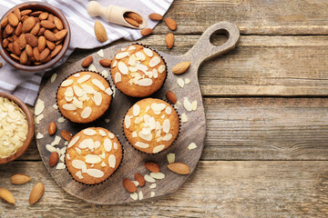Wall Mural - Tasty muffins with almond flakes and nuts on wooden table, flat lay. Space for text