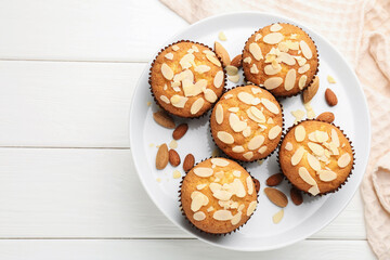 Wall Mural - Tasty muffins with almond flakes and nuts on white wooden table, top view. Space for text