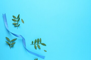 Wall Mural - Beautiful ribbon and green leaves on light blue background, flat lay. Space for text