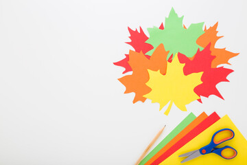 Wall Mural - Created colorful maple paper leaves, application paper, scissors and pencil on light gray table background. Closeup. Making autumn decoration. Flat lay. Empty place for text. Top down view.