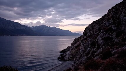 Wall Mural - Scenic view of a lake surrounded by mountains under a cloudy sky at dusk.