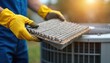 © Pete - Hands in yellow gloves hold dirty air conditioner filter. HVAC technician replaces old part for clean air. Home system maintenance improves indoor air quality, prevents allergens.