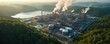 © Pete - Aerial view of large industrial complex with many pipes and towers next to vast lake. Steam plumes rise from factory chimneys into sky. Green hills surround manufacturing site during day.