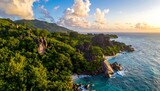 A scenic coastal landscape bathed in the golden light of sunset. Lush green vegetation meets the rocky shore and turquoise waters