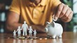 © Ada - Businessman putting coin on the piggybank and paper family on table, donation, saving, charity, family finance plan concept. person hand carefully places a coin into the slot