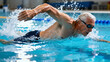 © Robert Garcia - Dynamic senior man with white hair swimming freestyle in a bright blue indoor pool, actively splashing water in an energetic and healthy lifestyle action shot.