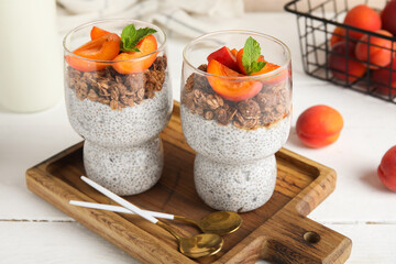 Wall Mural - Glasses of tasty chia seed pudding with granola and apricots on light wooden background