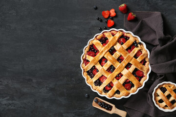 Wall Mural - Female hand and baking dishes with tasty berry pies on black grunge background