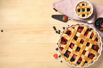 Wall Mural - Baking dishes with tasty berry pies and spatula on light wooden background