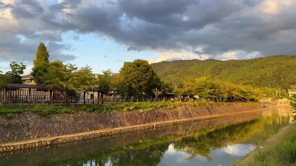 Wall Mural - Peaceful Kyoto canal with mountains, trees, reflecting water at sunset