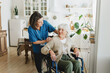 © shurkin_son - Smiling female nurse in blue uniform kneeling beside old woman in wheelchair, discussing treatment and test results. Friendly healthcare worker talking to disabled senior patient in medical office.