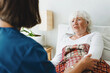 © shurkin_son - Anxious senior lady patient in bed at geriatric clinic looking with worried facial expression at her nurse sitting with her back turned to camera and comforting her before planned surgery