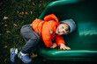 © Cavan Images - Smiling child in orange coat lying on a green playground slide