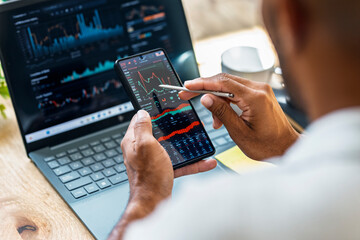 Trader analyzing stock market data at home office with smartphone and laptop