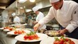 © Elena - Artistic plated gourmet meal with fresh tomatoes and herbs being arranged by a chef in a professional kitchen under warm lighting