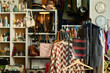 © pressmaster - Clothing rack displaying assorted vintage garments standing in foreground of thrift shop with shelves and racks filled with accessories, bags, and hats visible in background
