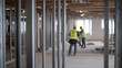 © photo for everything - Interior Construction in Progress: Metal framework under construction. Two workers wearing safety vests blurred in the background. Room in progress.