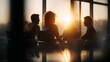 © Thares2020 - Three silhouetted professionals in an office engage in discussion during the golden hour illuminated by warm sunlight