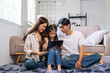 © amnaj - Parents and daughter sitting on living room floor enjoying educational content on a tablet, learning together