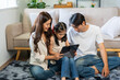© amnaj - Family parents and child sitting on floor rug, relaxing while watching and interacting with a tablet computer together