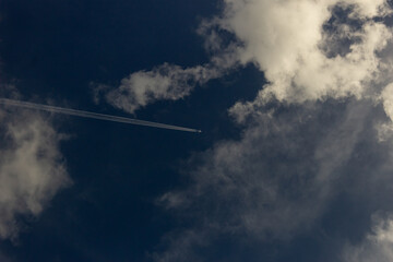 Wall Mural - Airplane in the blue sky with white clouds and plane trail.