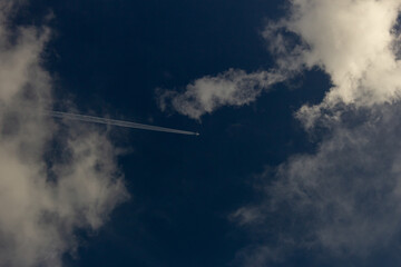 Wall Mural - Airplane in the blue sky with white clouds and plane trail.