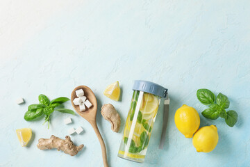 Wall Mural - Bottle of infused water with basil leaves, ginger, lemons and sugar cubes on light blue background