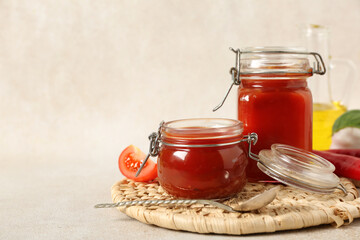 Wall Mural - Jars of tasty ketchup with fresh vegetables on light background