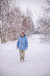 © StockMediaSeller - Elderly woman in a blue winter coat walking alone through a snowy countryside path. She looks up at the snow-covered trees around her, enjoying the calm and peaceful winter atmosphere.