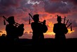 © Aleks - Silhouetted Musicians Playing Bagpipes Against a Dramatic Orange and Purple Sunset with Billowy Clouds in the Sky