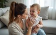 © hao - Indoor image of cute young female with ponytail holding tight her charming baby, sitting on sofa with him. Pretty mother and son bonding in living room, mom looking at child with love and tenderness