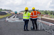 © kamonrat - Two railway engineers wearing safety helmets and reflective jackets inspect new rail track construction with surveying equipment.