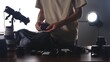 © kinomaster - A man organizing camera equipment on a table, including lenses and batteries, with studio lighting in the background.