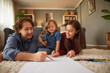 © Stockphotodirectors - A joyful family spends quality time together, lying on a soft carpet, drawing and painting. They share laughter and creativity in a warm living room setting.